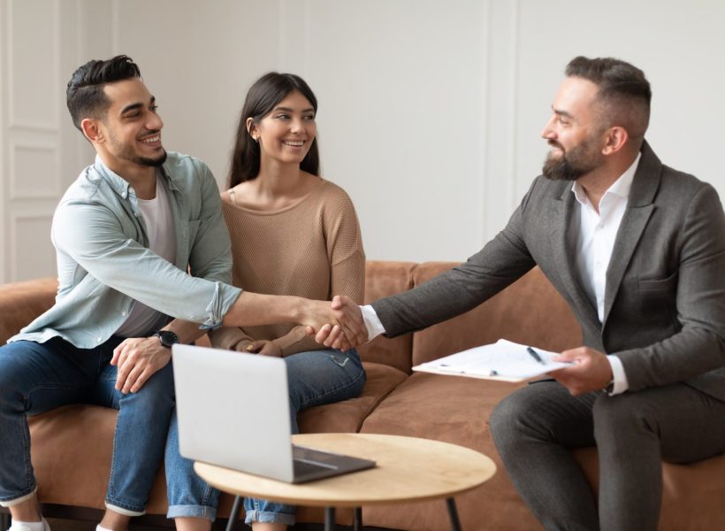 millennial-couple-buying-new-apartment-shaking-hands-with-realtor-e1658808851617.jpg